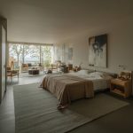 Modern bedroom with neutral colors, large bed with white sheets, abstract wall art, and tree views through large windows