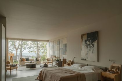 Modern bedroom with neutral colors, large bed with white sheets, abstract wall art, and tree views through large windows