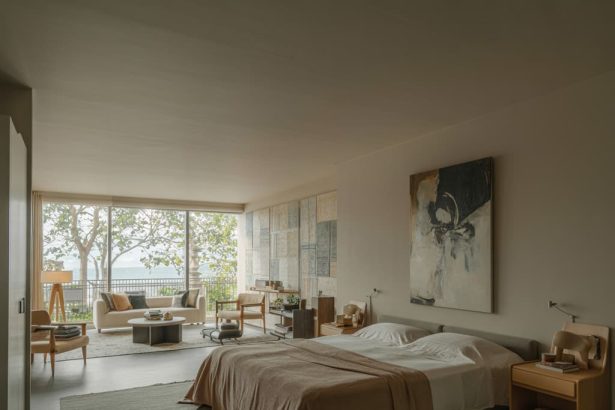 Modern bedroom with neutral colors, large bed with white sheets, abstract wall art, and tree views through large windows